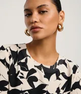 Blusa de manga corta con escote redondo y estampado floral abstracto en blanco y negro. Presenta costuras decorativas en contraste en el cuello y los puños.