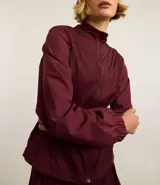 Campera deportiva femenina, modelo rompevientos, confeccionada en poliamida, con cuello alto y puños ajustados. Sin estampa, tiene cierre delantero con cremallera y recortes con hilo reflectante.