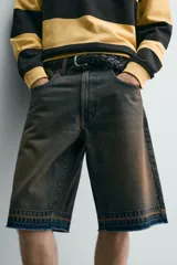 Bermuda de denim de algodón con efecto lavado desgastado en tonos marrones y azules. Tiene tiro medio, diseño de cinco bolsillos, pierna recta de corte holgado y bajo con acabado irregular. Cuenta con cierre frontal de cremallera y botón metálico.