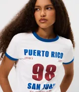 Remera de algodón con cuello redondo y mangas cortas, con vivos en color azul en cuello y mangas. Presenta una estampa frontal con la inscripción 'Puerto Rico 98 San Juan' en colores azul y bordó.