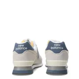 Championes urbanos New Balance modelo 574, color beige con detalles en azul marino y gris. Confeccionados en una combinación de gamuza y malla, cuentan con el logo N característico en los laterales, entresuela con tecnología ENCAP para mayor estabilidad y suela de goma.