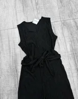 Mono largo negro de tejido arrugado con escote en V, sin mangas y corte holgado. Incluye cinturón de lazo en la cintura.