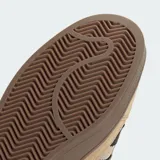 Championes Adidas Campus ST de estilo urbano inspirado en los años 90. Presentan un exterior de gamuza y lona en tonos marrones con las icónicas tres tiras laterales en color negro. Cuentan con suela de caucho resistente y cierre mediante cordones.