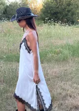 Vestido corto tipo lencero de seda color blanco, con detalles de encaje negro en el escote en V y en el ruedo asimétrico. Presenta breteles finos ajustables y una caída fluida.