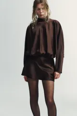 Vestido corto de tejido satinado color marrón chocolate, con cuello subido y lazada tipo foulard integrada. Presenta mangas largas amplias, detalle de frunces en la cintura y cierre lateral con cremallera oculta.