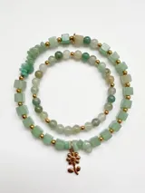 Set de dos pulseras de piedras naturales en tonos verdes y cuentas doradas, una de ellas con un dije colgante en forma de flor dorada.