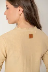 Polera de manga larga color beige con textura acanalada, cuello redondo y detalle de volados en el ruedo y los puños.