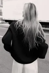 Jersey de punto negro, con cuello en V (pico) y manga larga, acabado en rib en puños, cuello y bajo.