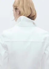 Chaqueta crop de denim blanco, confeccionada en algodón con un toque de elastano. Presenta cuello de solapa, cierre frontal con botones metálicos, bolsillos de parche con solapa en el pecho y manga larga con puños abotonados.
