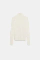 Jersey de punto liso en color beige, con cuello alto y manga larga con detalle de botones metálicos en los puños.