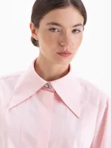 Camisa de poplín de algodón con corte holgado y largo hasta la cadera. Presenta cuello clásico con detalle de herraje metálico, cartera oculta con botones al tono y puños anchos con botones.