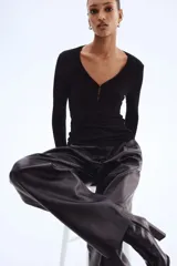Top negro de manga larga en tejido de punto acanalado fino. Presenta un escote en V profundo con una pequeña abertura frontal cerrada con dos corchetes ocultos.