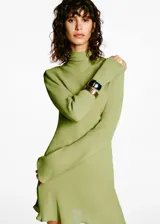 Vestido corto de color verde oliva, confeccionado en tejido fluido con cuello alto y mangas largas acampanadas. Presenta un diseño evasé que aporta movimiento a la prenda.