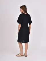 Vestido midi de color negro con cuello en V y mangas cortas tipo kimono. Presenta un corte holgado con cintura ligeramente marcada y falda con vuelo.