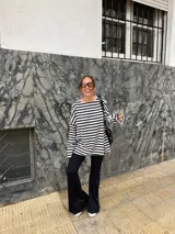Conjunto compuesto por remera de manga larga oversize a rayas horizontales blancas y negras con escote bote, y pantalón negro de corte flared.