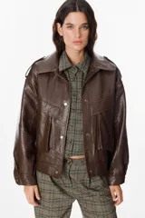 Chaqueta de cuero sintético con textura granulada, corte oversize, cuello camisero, cierre frontal con botones a presión, bolsillos frontales tipo cargo y detalles de charreteras en los hombros.