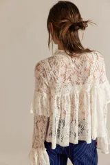 Top de encaje calado blanco, de corte corto y diseño amplio, con cuello alto, canesú frontal, volados superpuestos en el pecho y mangas largas acampanadas con detalle de volados.