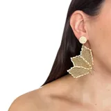 Aros colgantes con forma de flor tramada en mostacillas color dorado y blanco.