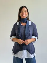Sweater de punto azul con diseño asimétrico y detalles bordados, que incluye una bufanda a juego y una camisa blanca de lino debajo.