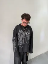 Remeron oversize de algodón pesado color negro con estampado gráfico en serigrafía gris en el frente y en ambas mangas. Presenta cuello redondo y grifa de la marca en el puño.