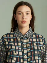 Camisa de viscosa con estampado a cuadros de estilo retro en tonos beige, azul marino, celeste y rojo. Presenta cuello camisero, cierre frontal con botones metálicos plateados y diseño con capas superpuestas en el pecho de inspiración country.