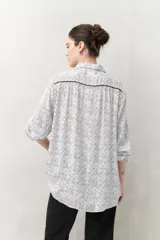Camisa de manga larga confeccionada en 100% viscosa, color blanco con estampado de rayas finas negras. Presenta cuello camisero, botones frontales negros y detalles de ribete negro en los hombros.