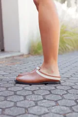 Mules de cuero color tostado con detalle de tira beige en el empeine y suela negra.