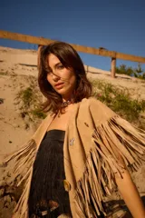 Chall de gamuza natural con diseño de flecos largos en todo el borde y detalle de pins metálicos decorativos en la parte frontal.