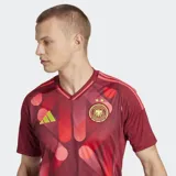 Camiseta de fútbol Adidas de la segunda equipación de la selección femenina de Alemania, color rojo oscuro con un estampado abstracto en tonos rojos y rosados. Presenta cuello redondo y detalles en amarillo neón en el logo y el escudo.