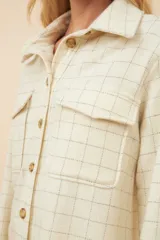 Camisa estilo leñador color beige con textura en espiga, de manga larga, con cuello clásico, cierre frontal con botones, dos bolsillos de parche con solapa abotonada en el pecho y puños abotonados. Confeccionada en lana fina sin teñir.