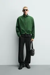 Campera verde oscuro de corte cropped y tejido técnico, con cuello alto, cierre frontal de cremallera con tirador circular, bolsillos ribeteados y puños y dobladillo elásticos.