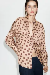 Camisa de corte clásico confeccionada en tela satinada, con estampado de lunares en contraste. Presenta cuello solapa, cierre frontal con botones y mangas largas con puños rectos.
