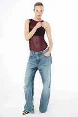 Body sin mangas de cuello redondo, confeccionado en una combinación de tul transparente y paneles de tela opaca a tono. Presenta un diseño ajustado con cierre inferior mediante botones a presión.