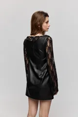 Vestido corto de símil cuero negro, de corte recto, escote amplio y sin mangas, combinado con mangas largas de encaje negro.
