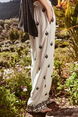Pantalón color crema de tiro medio con cintura elástica ajustable y bolsillos delanteros. Presenta bordados florales en negro y corte ancho.
