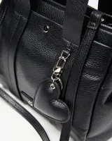 Cartera mediana de cuero sintético negro con textura granulada, doble asa de mano, correa ajustable y desmontable, y llavero colgante en forma de corazón.