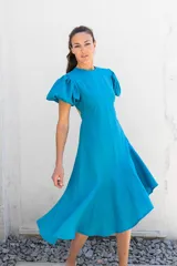 Vestido azul con escote redondo, mangas cortas abullonadas con elástico, espalda descubierta y largo asimétrico.