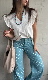 Musculosa blanca de diseño ligero con escote en V y sutiles detalles bordados tonales en el frente, complementada con volados en las sisas.