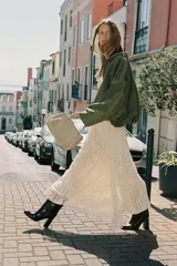 Falda midi color crema o blanco roto, confeccionada en tejido de encaje con forro interior a tono. Presenta cintura elástica y se complementa con un cinturón tipo cadena metálica dorada con caída.