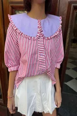 Camisa de lino texturado con diseño a rayas verticales rojas y blancas, cuello babero desmontable en color lila con volados y mangas cortas abullonadas.