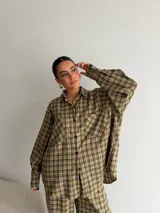 Camisa de corte oversize confeccionada en tela de viyela con estampado de cuadros en tonos verdes y marrones. Presenta cuello clásico, cierre frontal con botones, mangas largas con puños abotonados y dos bolsillos frontales con solapa.