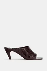 Sandalia tipo mule de tacón alto, color marrón oscuro con textura de piel de cocodrilo. Presenta punta cuadrada y un diseño abierto en la parte delantera.