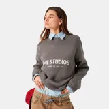 Sweater gris de punto con cuello redondo y mangas largas. Estampado frontal con el logo 'EME STUDIOS curated by ben ice' en color blanco.