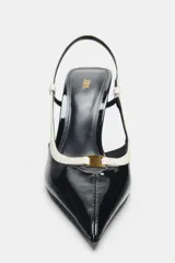 Zapatos de tacón alto fino y destalonados, con acabado efecto acharolado en color negro y detalles en blanco combinados en las tiras y el borde. Presentan puntera fina.