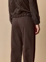 Pantalón de corte relajado color marrón, confeccionado en una mezcla de algodón y elastano. Presenta costuras en contraste color rojo en bolsillos y bragueta, con cierre de botón metálico.