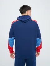 Canguro deportivo Umbro del Club Nacional de Football, modelo Nexo para hombre. Diseño en color azul marino con mangas rojas y detalles en celeste y blanco, capucha con cordón ajustable y bolsillo tipo canguro.