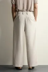 Pantalón relaxed fit de color blanco off-white, confeccionado en tejido con lino. Cuenta con pliegues frontales en la cintura, bolsillos delanteros y cierre frontal con cremallera y botón.
