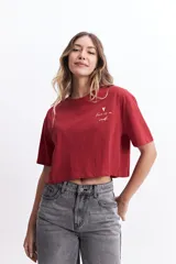 Remera corta (cropped) de algodón color verde lima, con cuello redondo y manga corta. Presenta un pequeño estampado en el pecho con un corazón naranja y texto manuscrito.