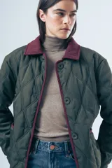 Campera acolchada de diseño matelasse con pespuntes ondulados, cuello clásico en contraste y cierre frontal con botones. Presenta bolsillos frontales con ribetes a tono y calce relajado.