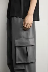 Pantalón jogger de corte relajado confeccionado en tejido de algodón compacto con elasticidad. Presenta cintura elástica ajustable con cordón, bolsillos laterales, bolsillos cargo con solapa en las piernas y detalle de pliegues en las rodillas.